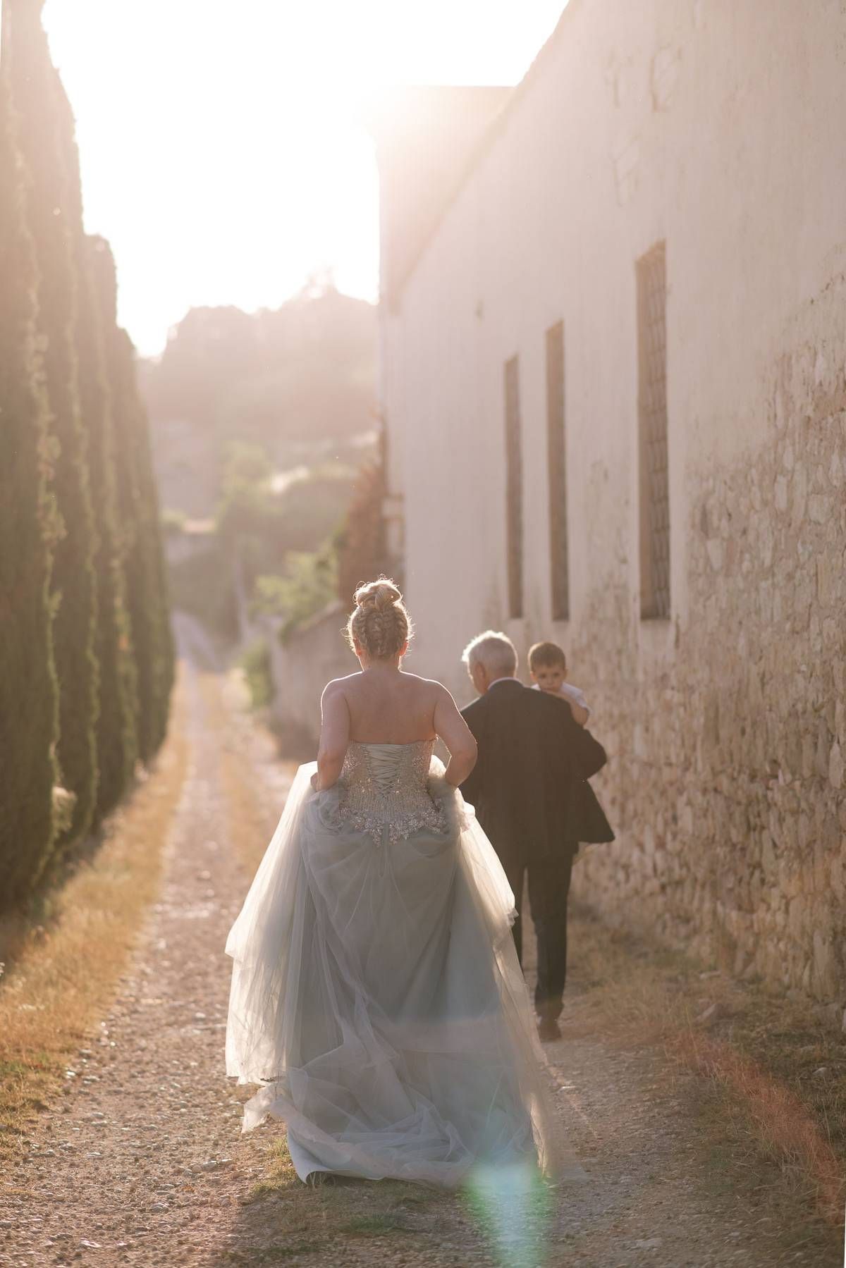 A dreamy wedding scene with backlit figures walking down a tree-lined pathway at sunset.