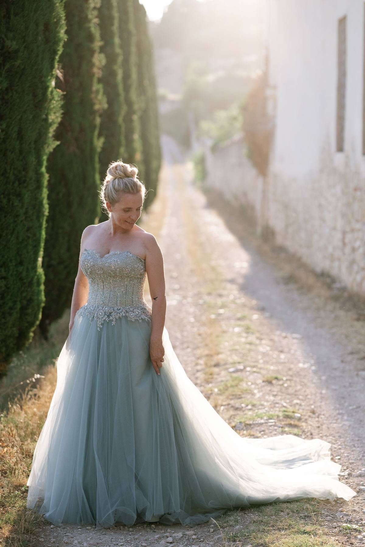 A powder blue wedding gown with beaded bodice photographed in golden sunlight along a cypress-lined path.