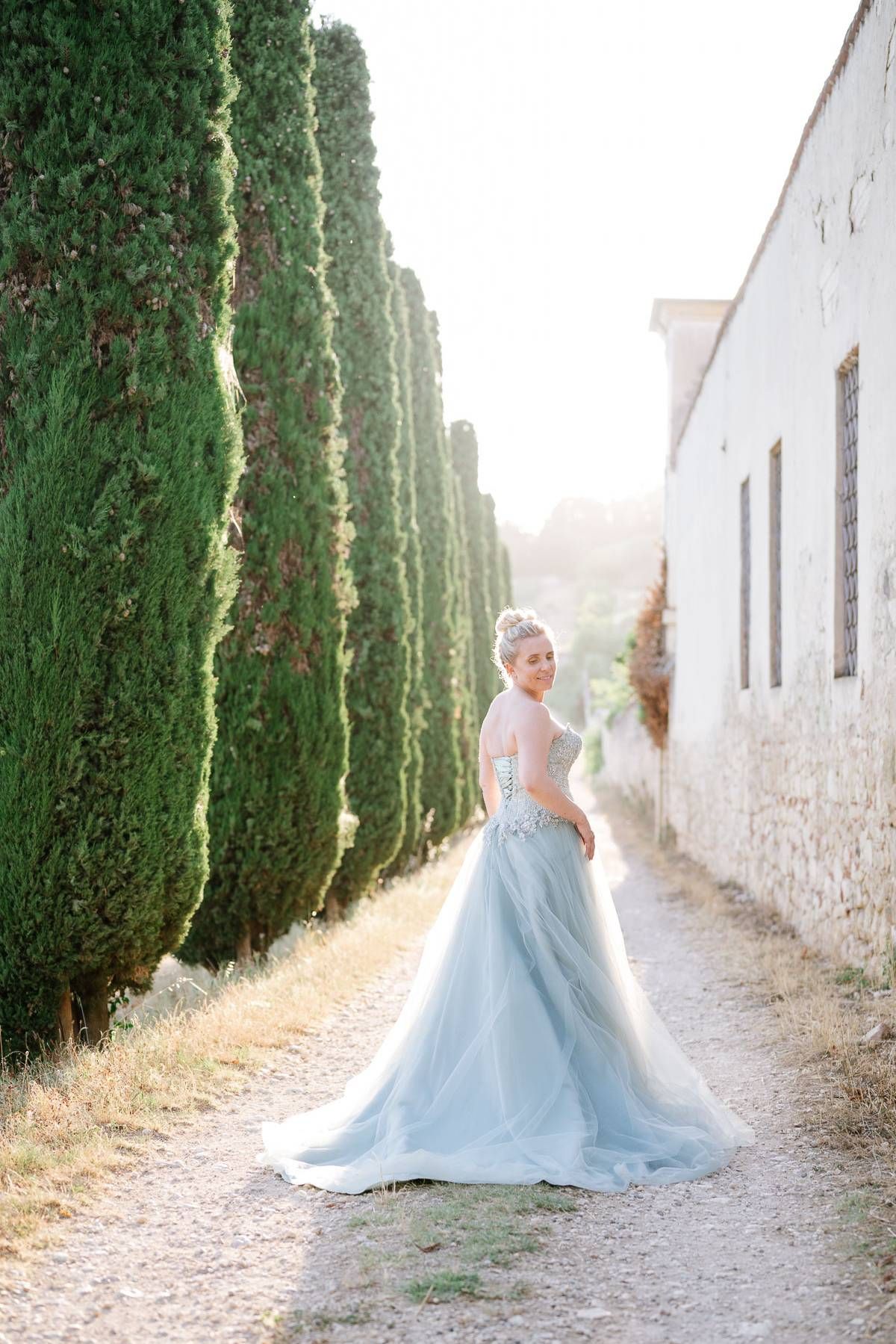 An ethereal bridal portrait featuring a light blue gown against a backdrop of tall cypress trees.