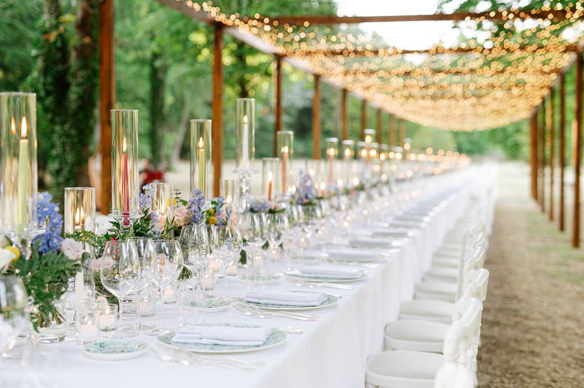 An elegant outdoor wedding table setting with string lights and floral centerpieces.