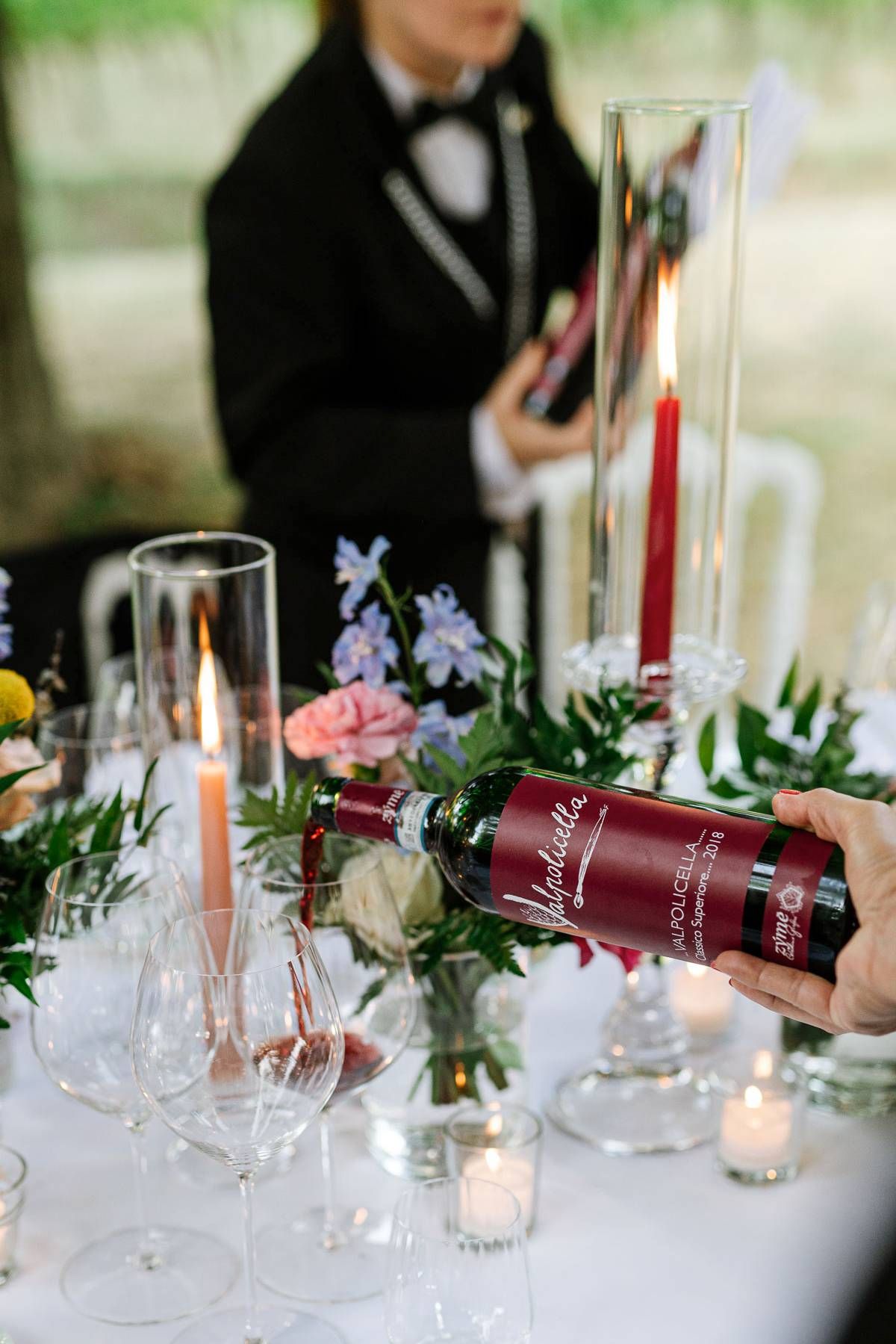 Elegant table setting with red wine bottle, candles and delicate floral arrangements.