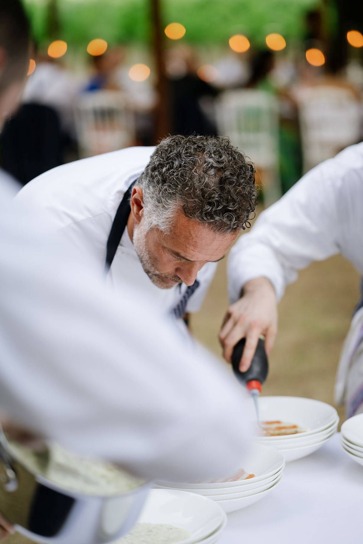 Chef in white uniform carefully plates dishes during outdoor service.