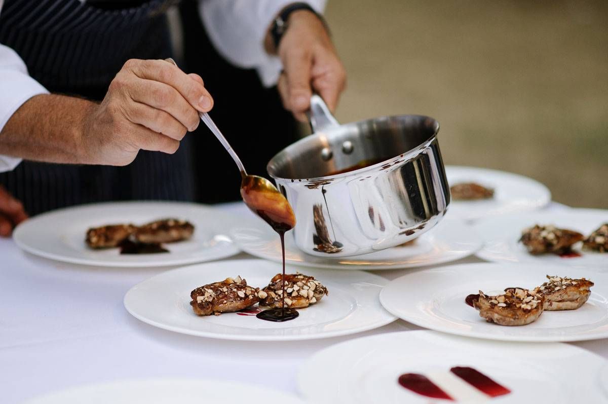 Chef drizzles sauce over plated dishes at an elegant catering event.