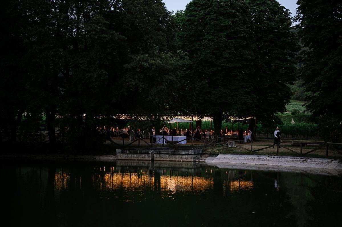 Evening outdoor reception by a serene pond with string lights reflecting on water.