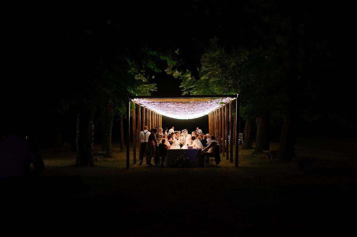 Illuminated outdoor wedding reception tent glows warmly in dark wooded setting.