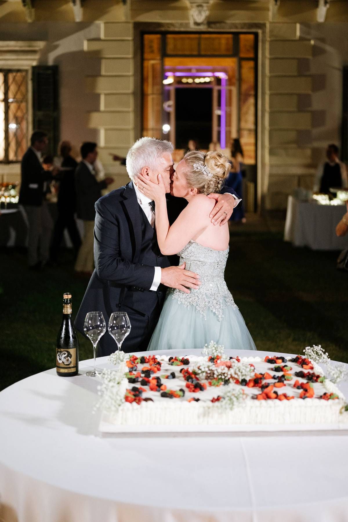 Couple shares intimate moment at wedding cake table decorated with flowers and candles.