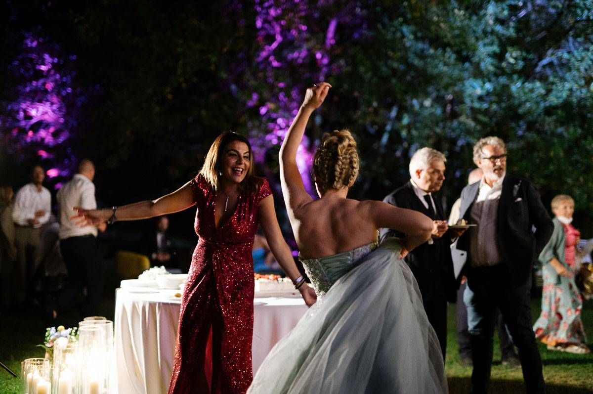 Outdoor wedding reception with guests dancing and celebrating under purple lighting.