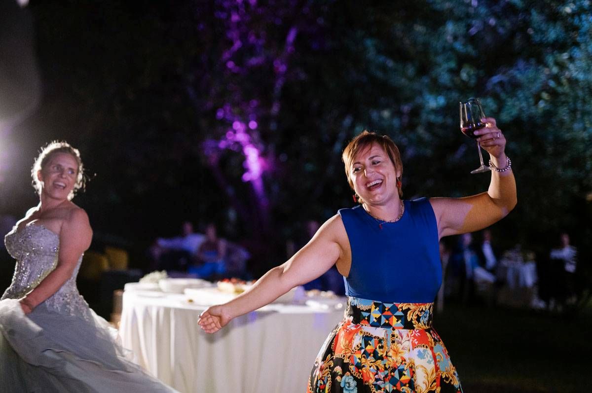 Wedding guests dancing enthusiastically during an outdoor evening reception with purple uplighting.