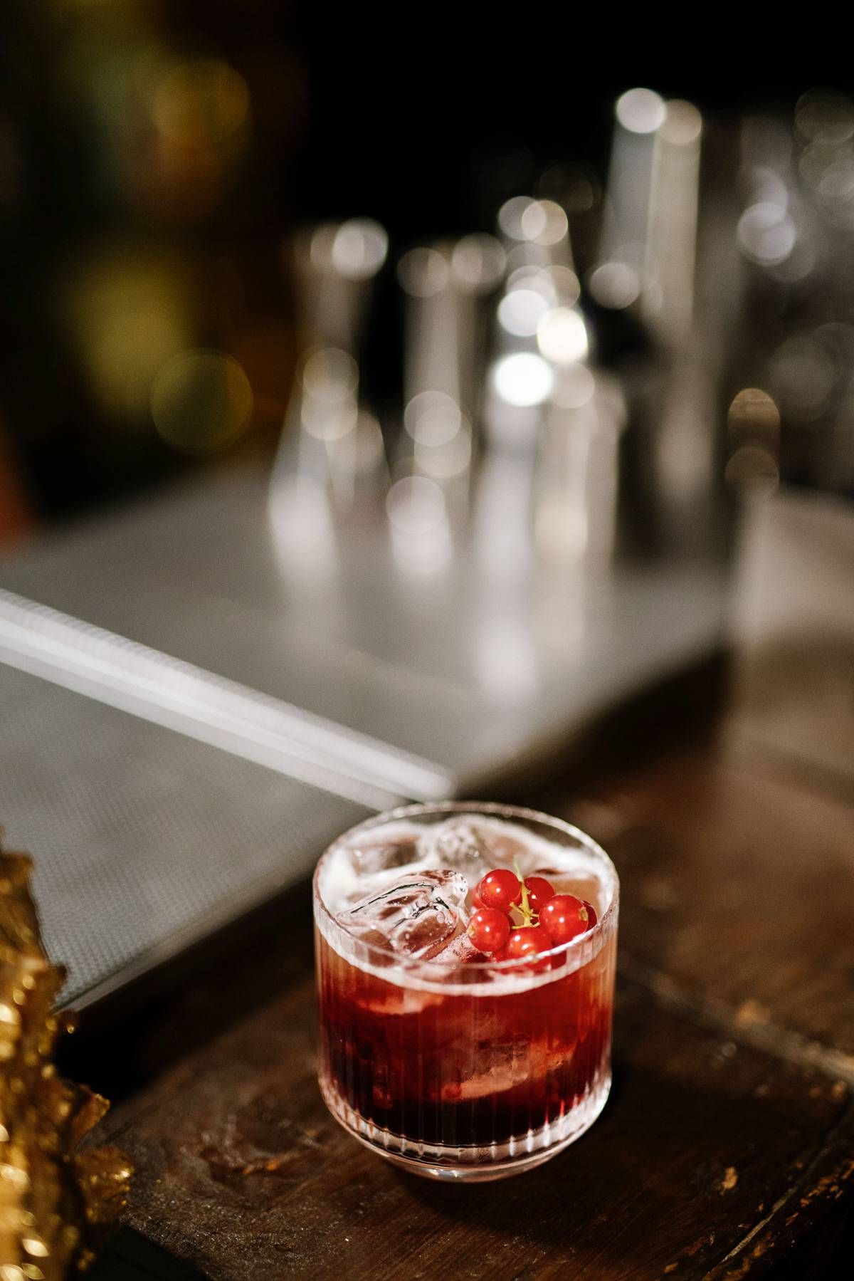 Red cocktail with ice and berry garnish on a dark wooden surface.