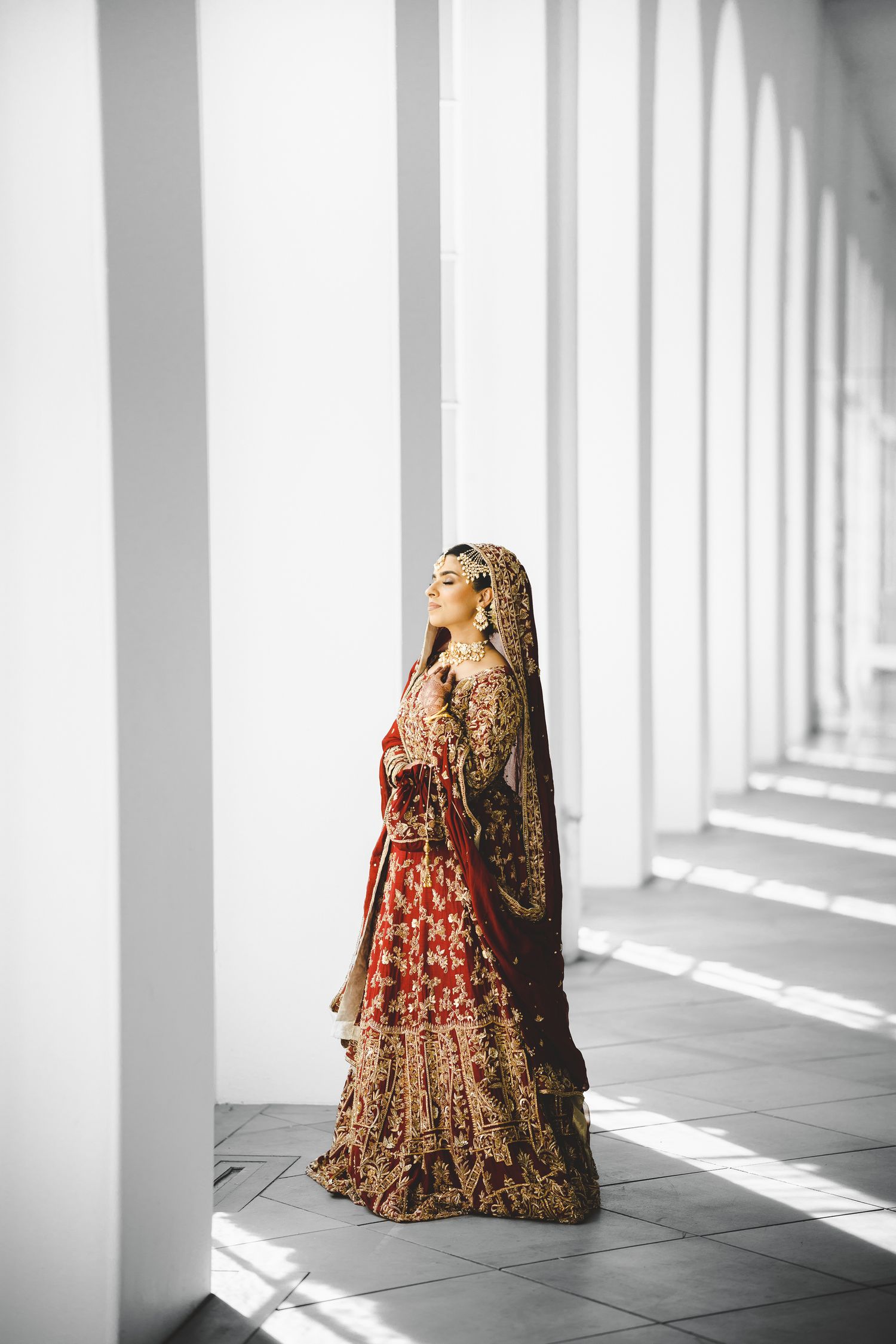 Traditional South Asian bridal outfit photographed in a modern hallway with dramatic shadows and light.