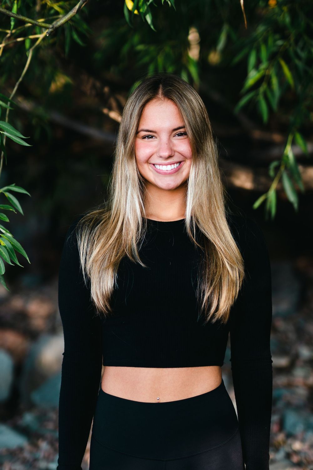 Portrait of person in black crop top smiling outdoors with natural lighting.