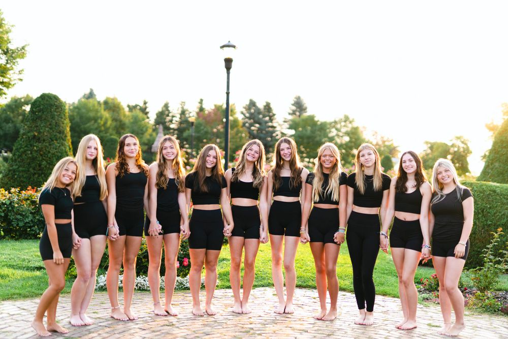Group of dancers in matching black outfits posing together outdoors.