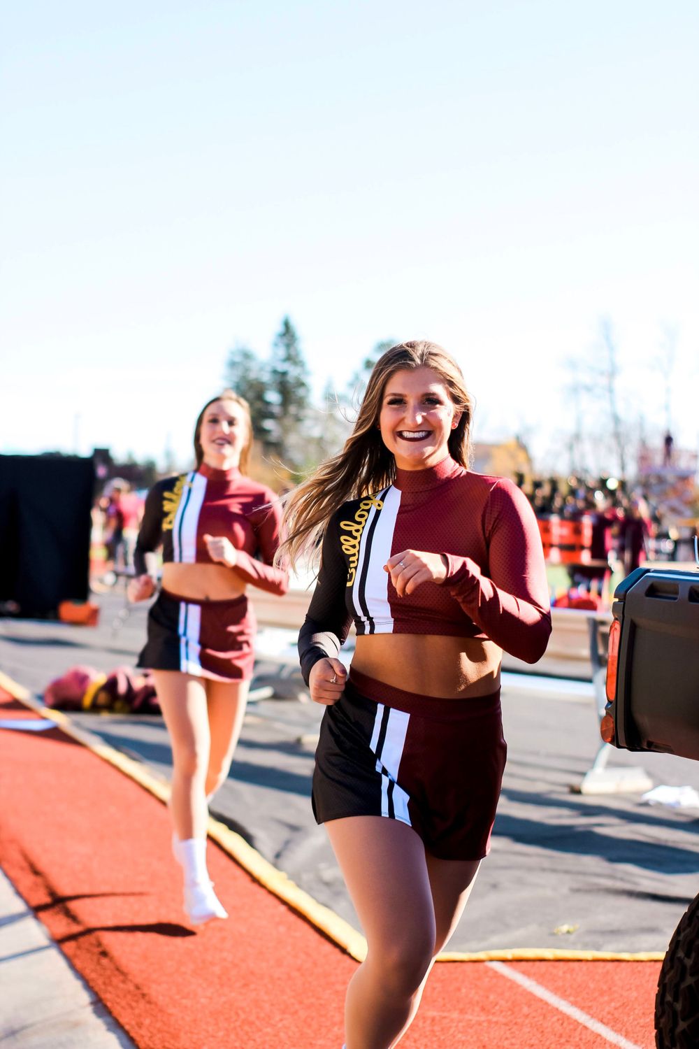 Athletes in maroon and black uniforms running on a red track during an outdoor sporting event.