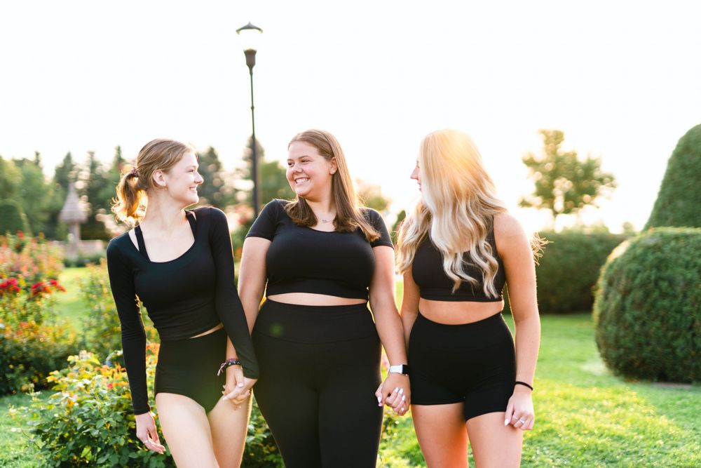 Three friends in matching black outfits laughing together in a garden at sunset.