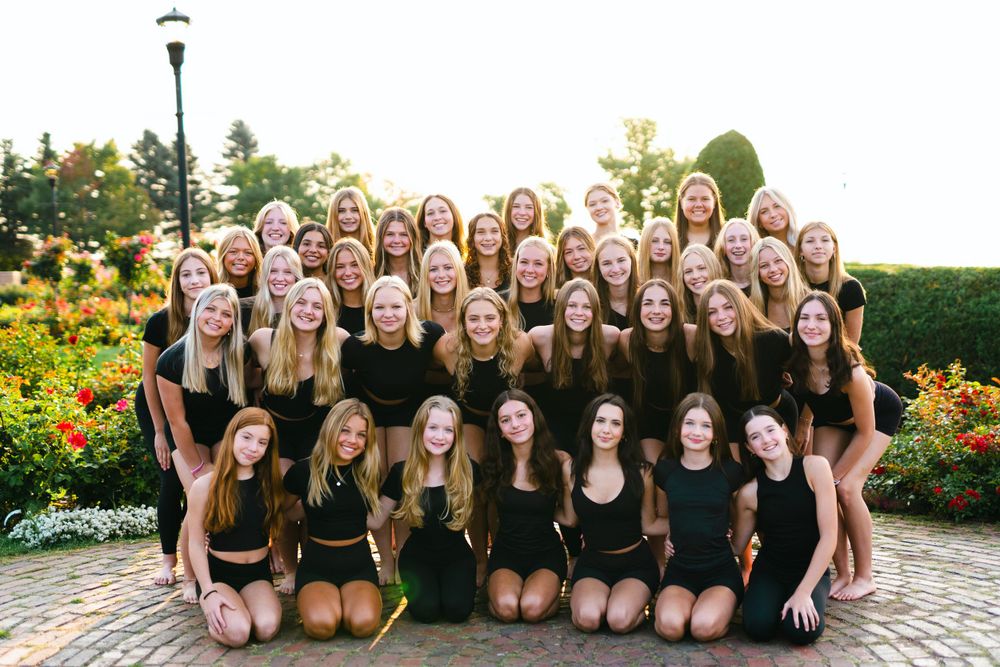 Large group in matching black outfits posing together in garden setting.