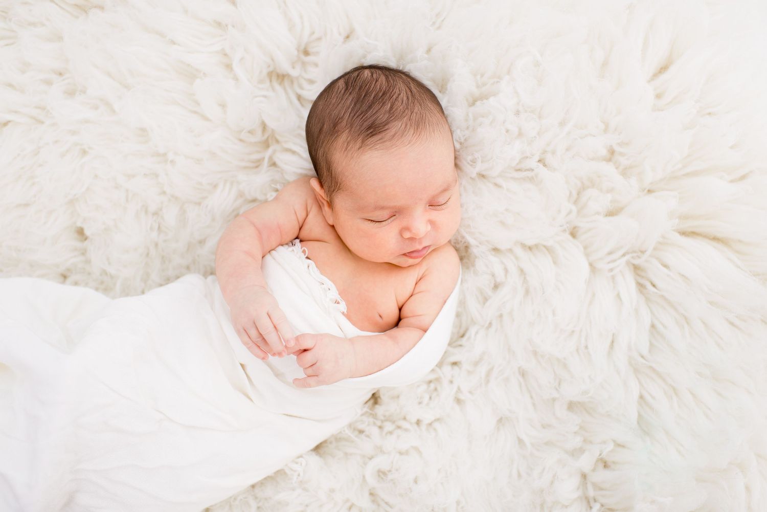 Newborn baby sleeping peacefully on cream-colored plush blanket.