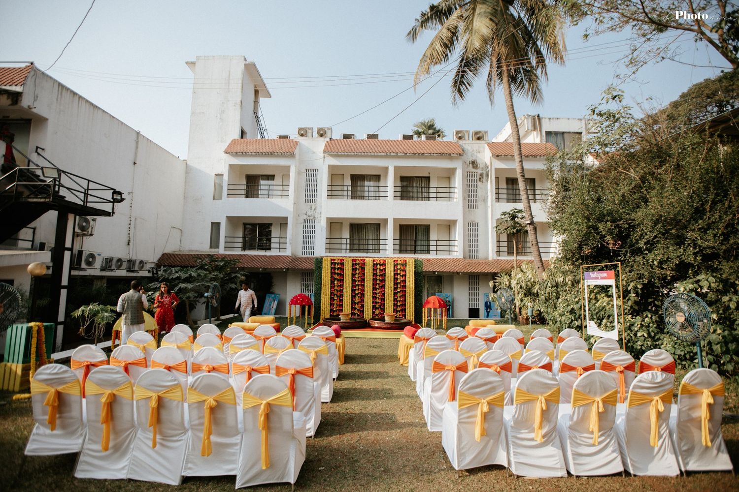 Outdoor wedding venue with white chairs and peach sashes arranged in rows under palm trees.