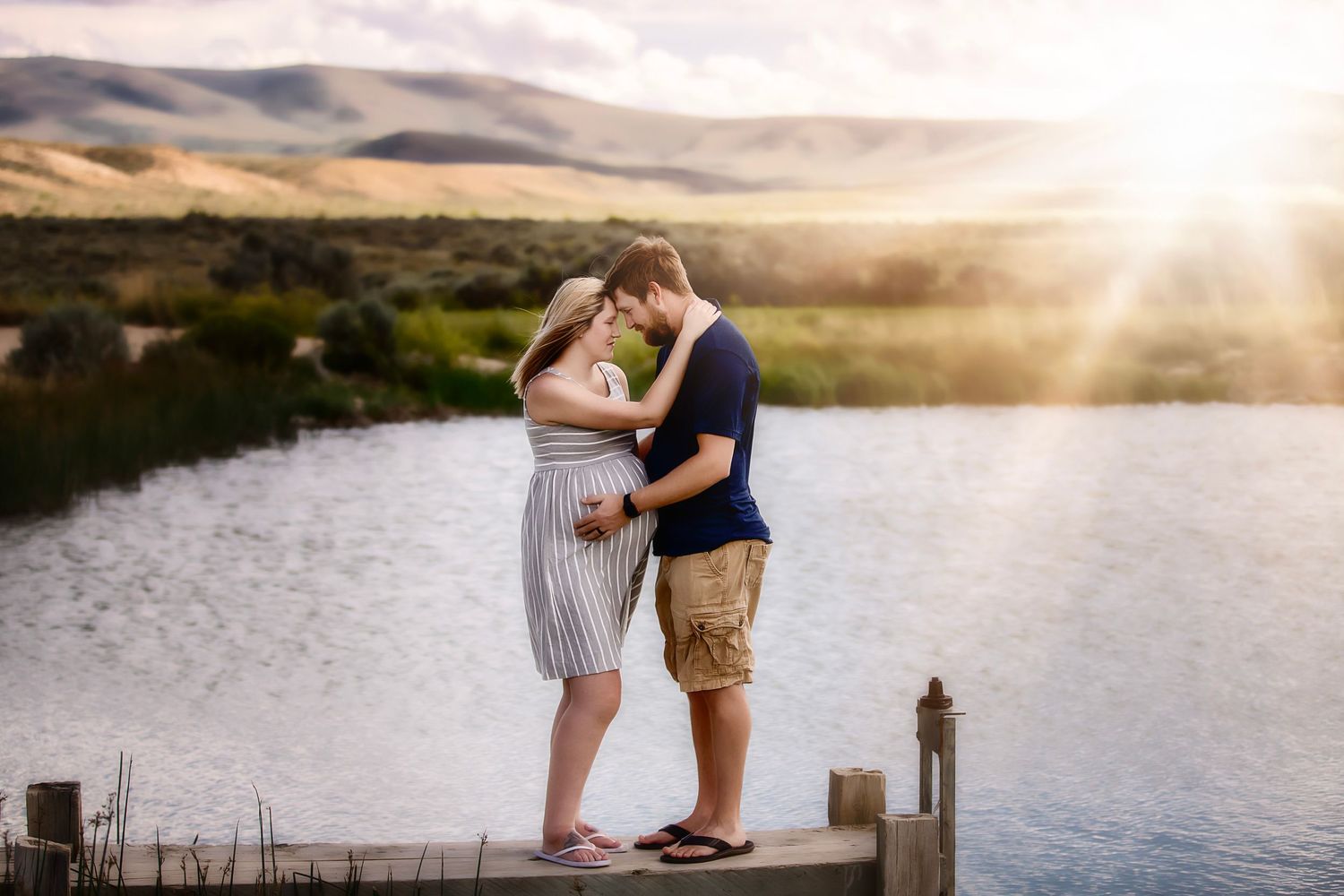 A romantic sunset moment between a couple standing on a dock overlooking a lake.