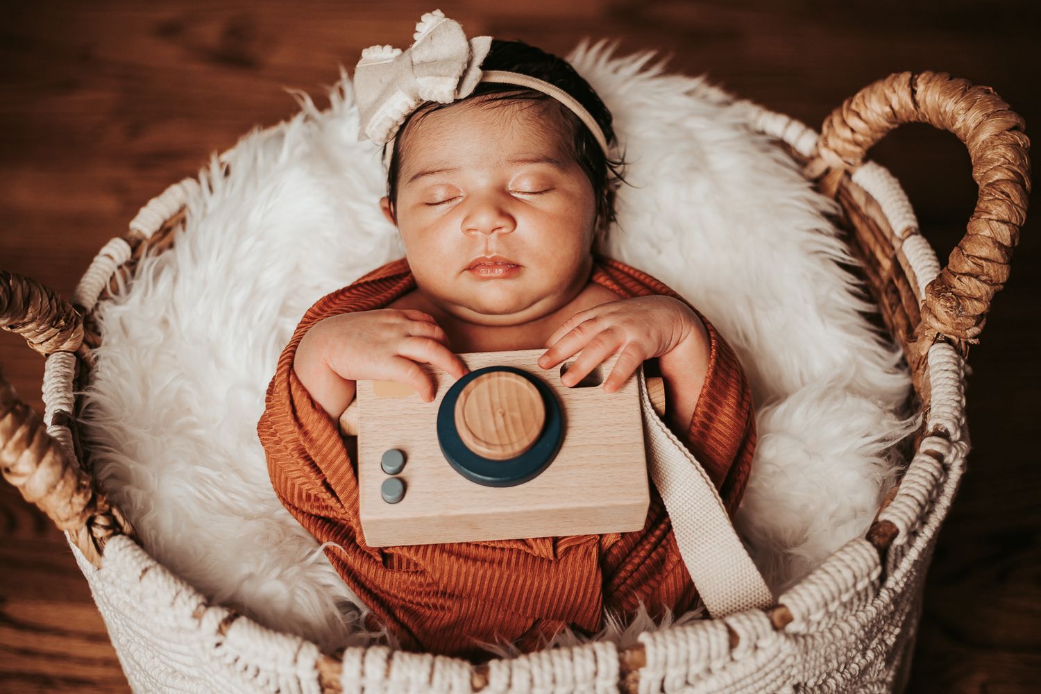 Newborn baby sleeping peacefully in a cozy white fur-lined basket.