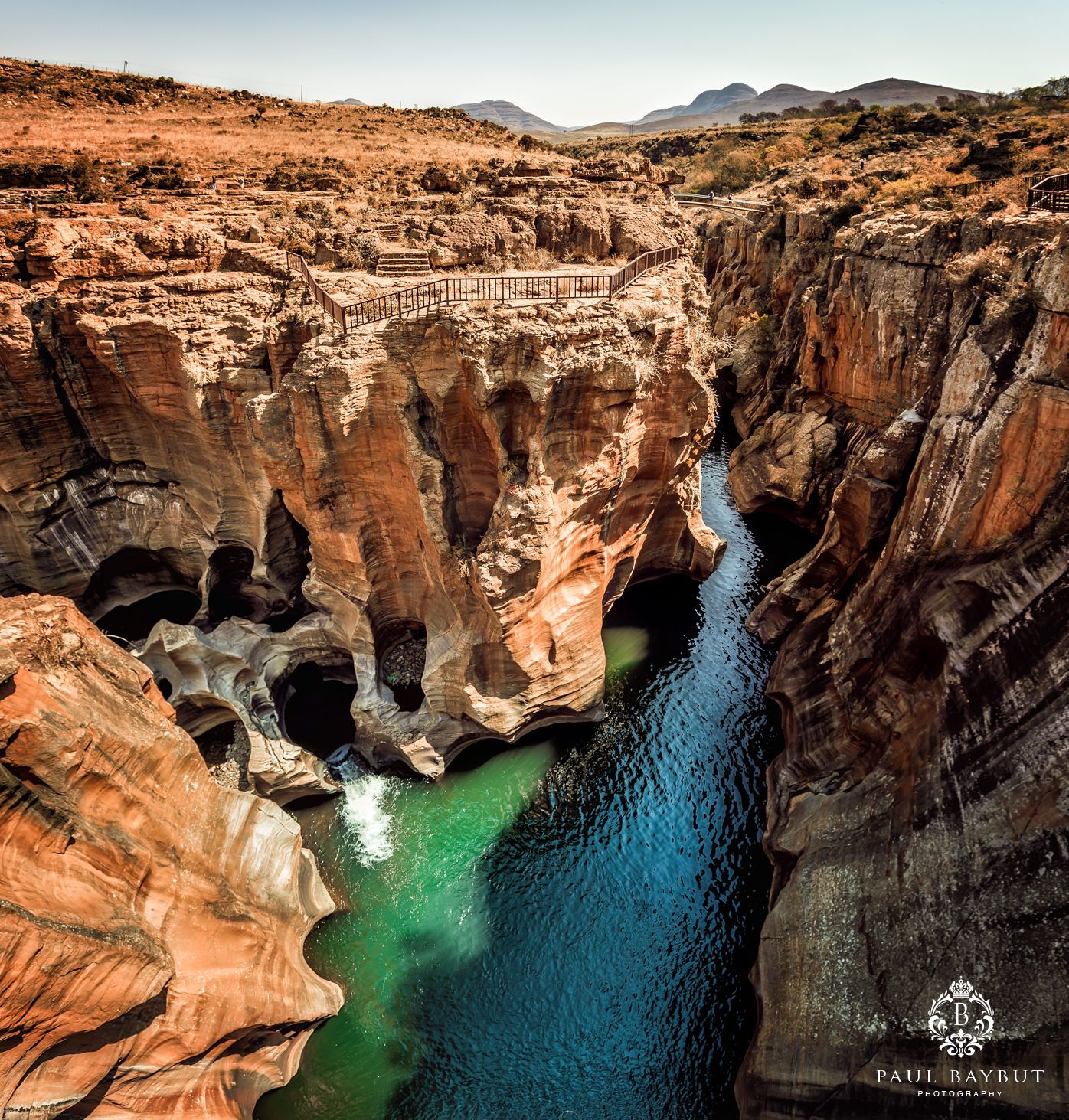 Dramatic canyon landscape with turquoise water flowing between red rock cliffs and curved formations.