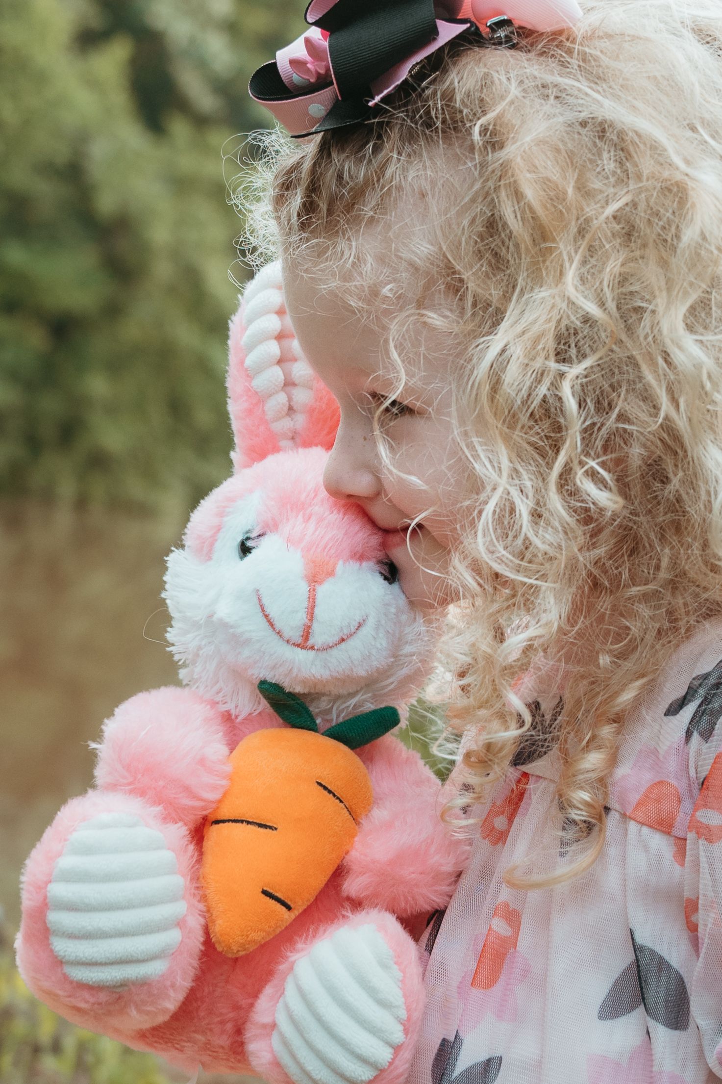Soft profile view of a child with curly blonde hair holding a pink plush bunny with a carrot.