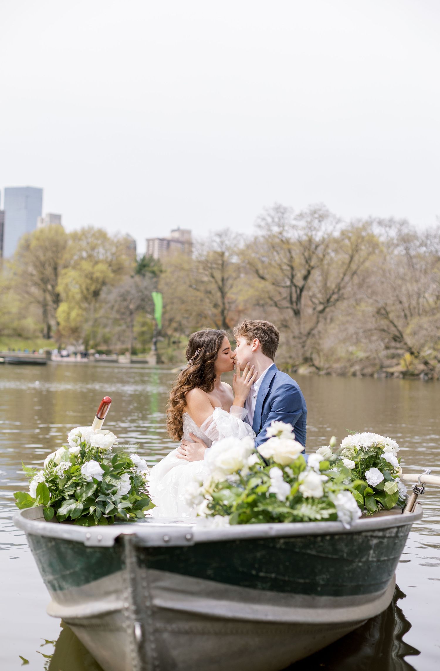 Romantic wedding couple shares intimate moment in rowboat decorated with white floral arrangements on Central Park lake.