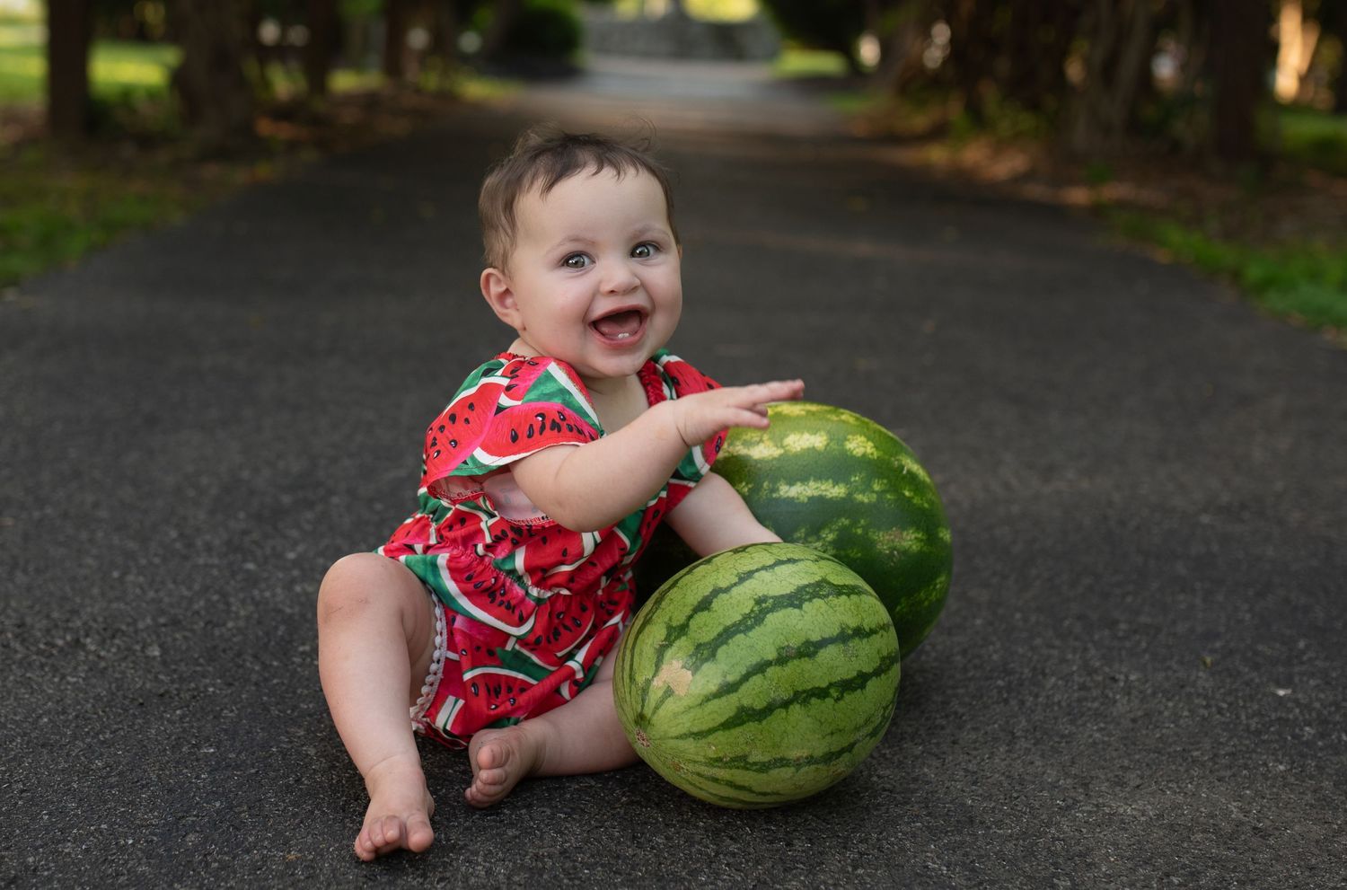 Baby girl in a watermelon rompers posing beside two large watermelons