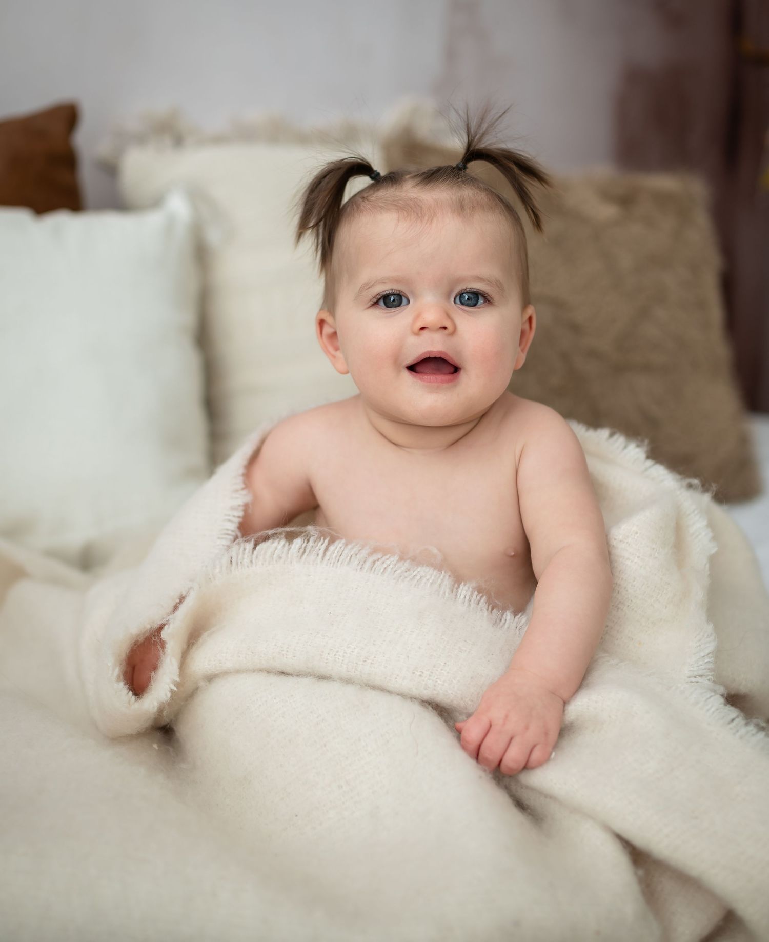 Baby girl with pigtails smiling and sitting on a bed