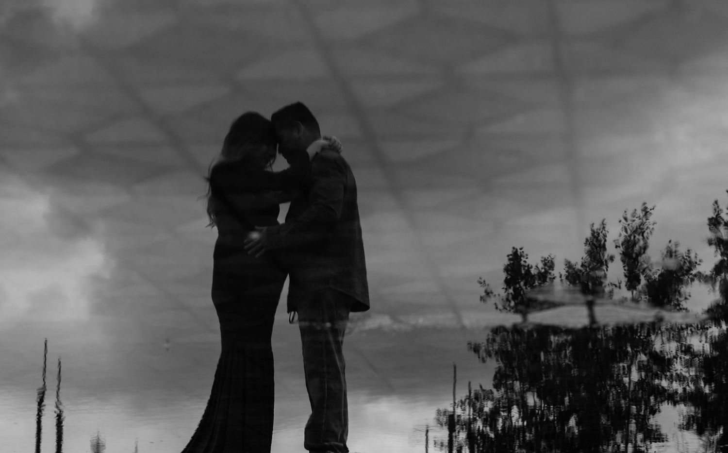 Reflection of Pregnant woman and her partner in a loving embrace in a puddle