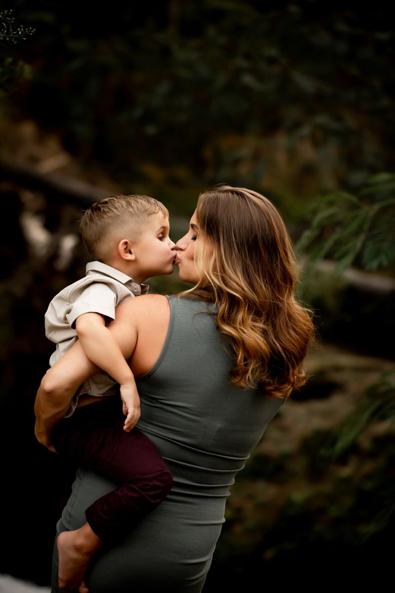 Pregnant woman in a green dress holding her oldest son giving him a kiss.