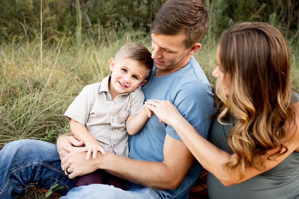 Family of 3 sitting in a field playing with soon to be big brother.