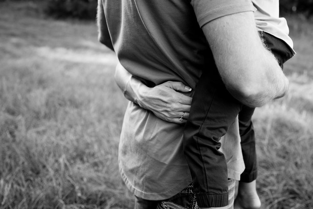 Black and white image of mom's arm wrapped around her husband while he's holding their little boy.