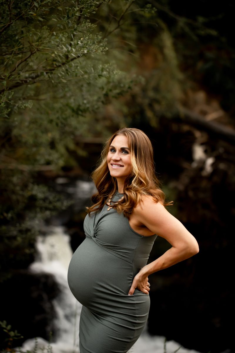 Pregnant woman posing in green dress in front of waterfall at Savannah River Rapids.