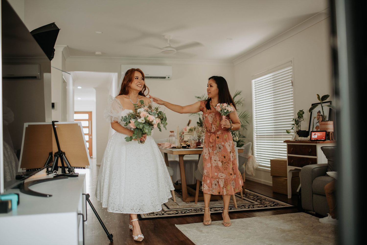 Bride in white dress celebrates with friend in floral dress.