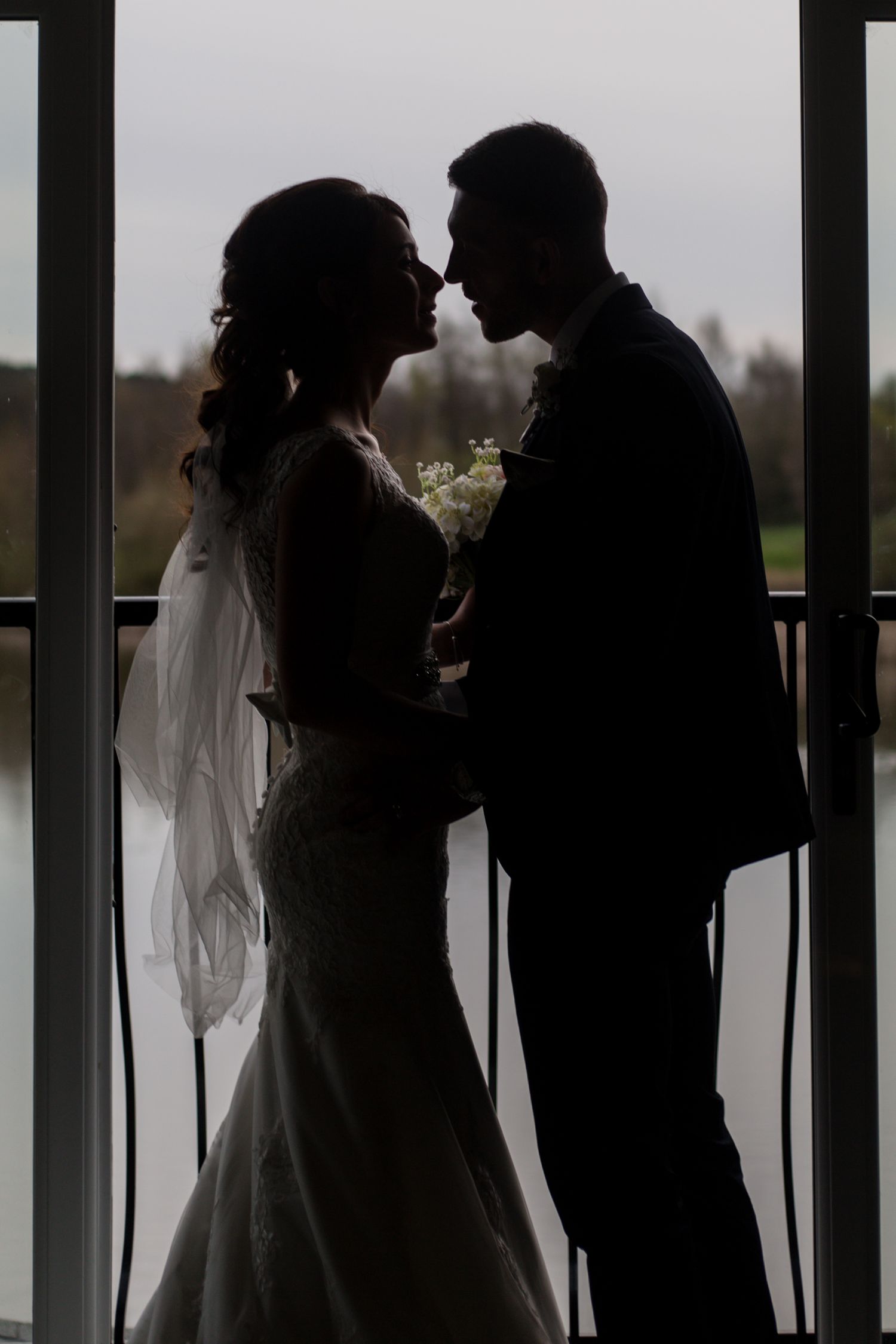Romantic silhouettes of bride and groom against window backdrop.