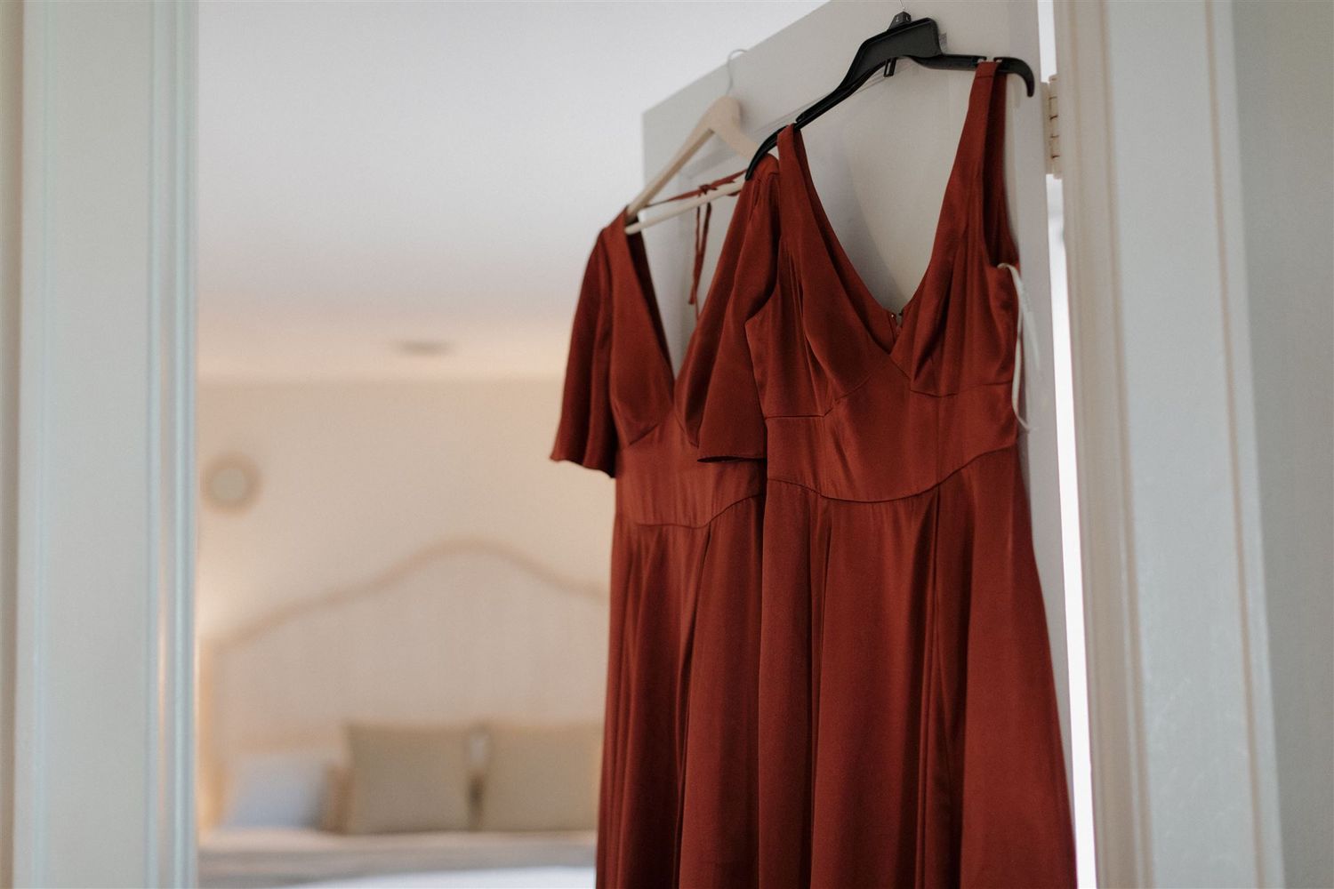 A burgundy bridesmaid dress hangs on display against a white wall.
