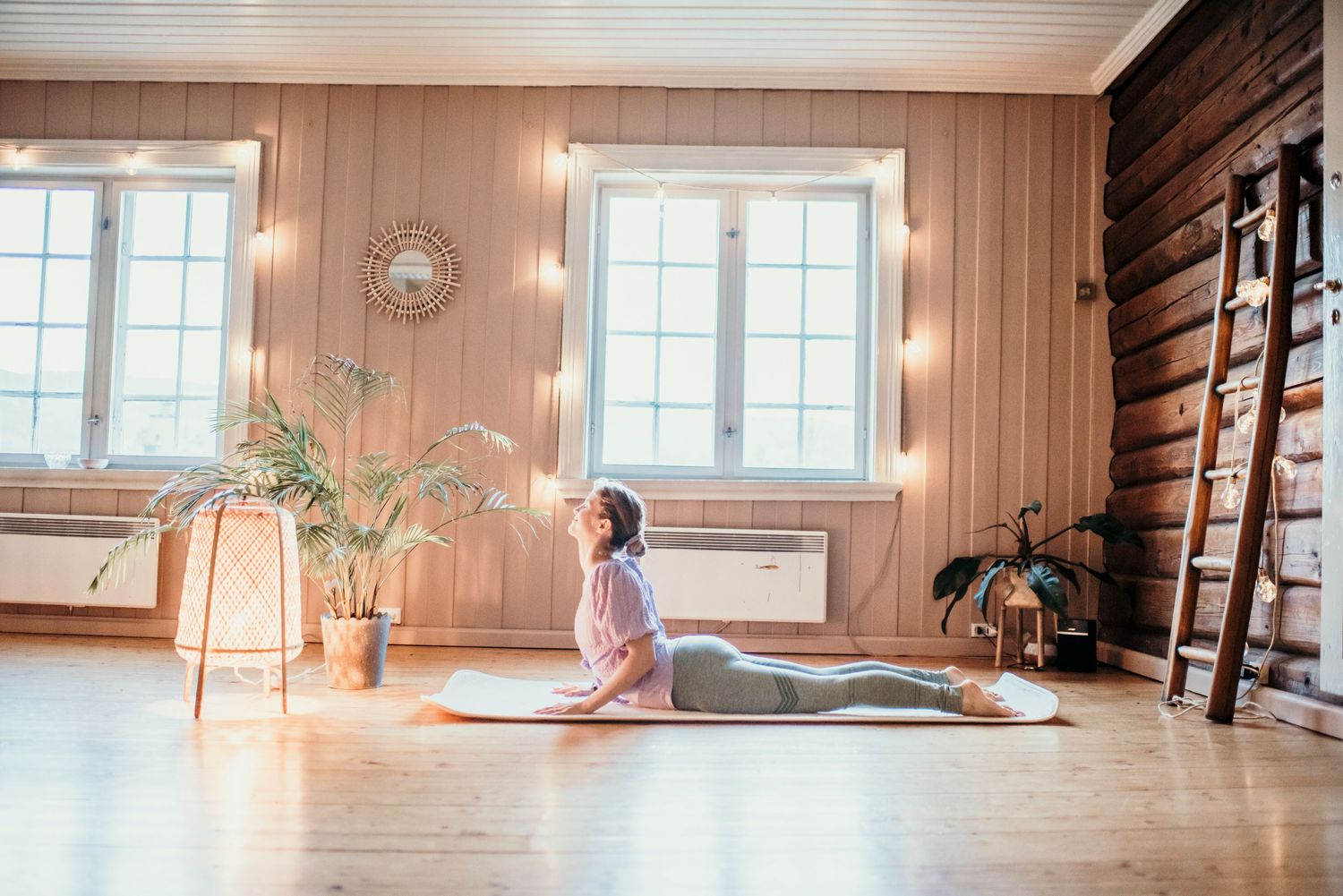 Yoga cobra pose practiced in a bright sunlit room with wooden walls and exercise equipment.