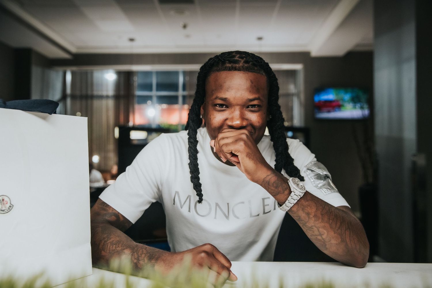 Portrait of someone in a white Moncler shirt smiling at a table.