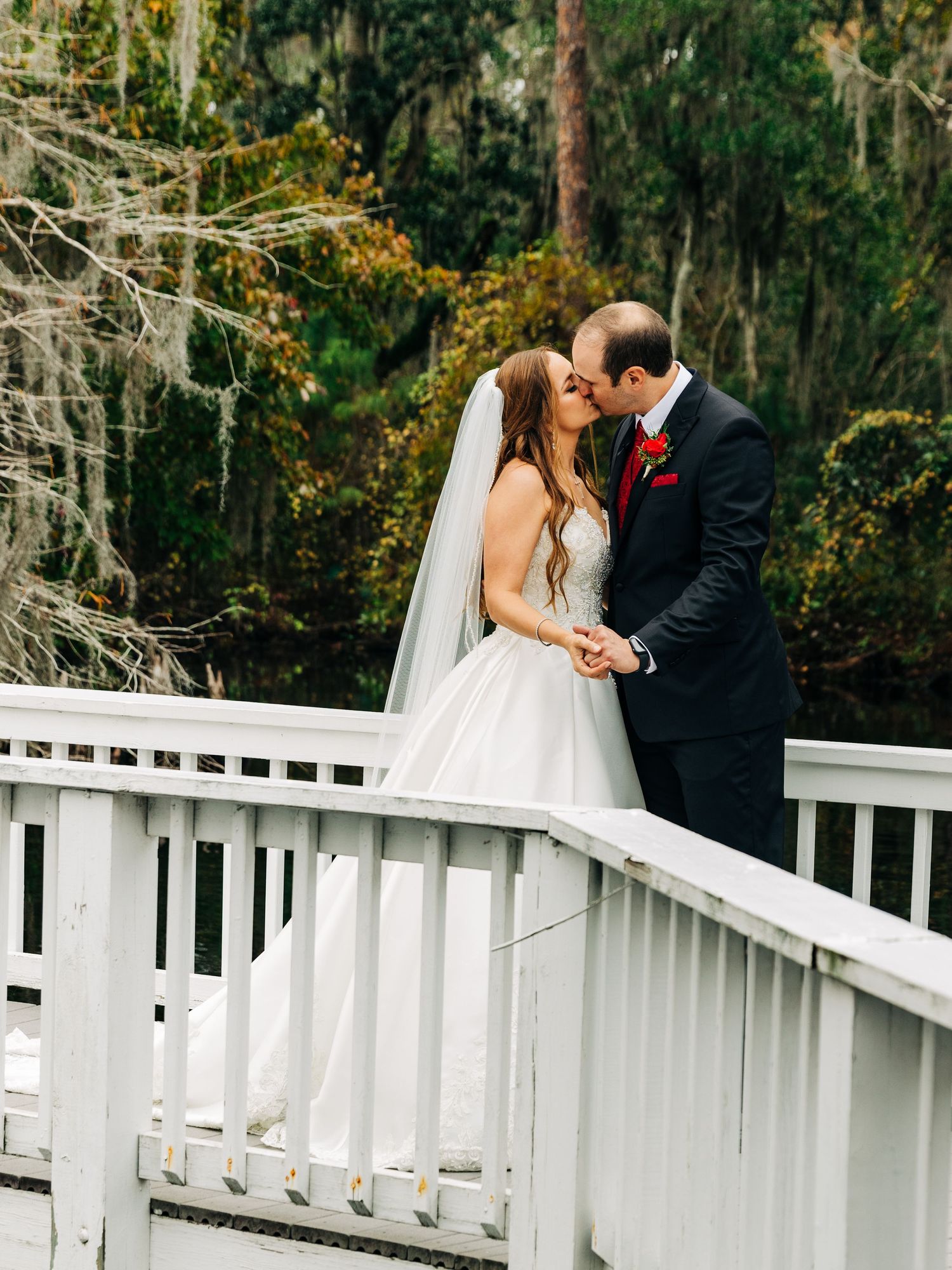 Romantic wedding couple sharing a tender moment on a white bridge surrounded by Spanish moss.