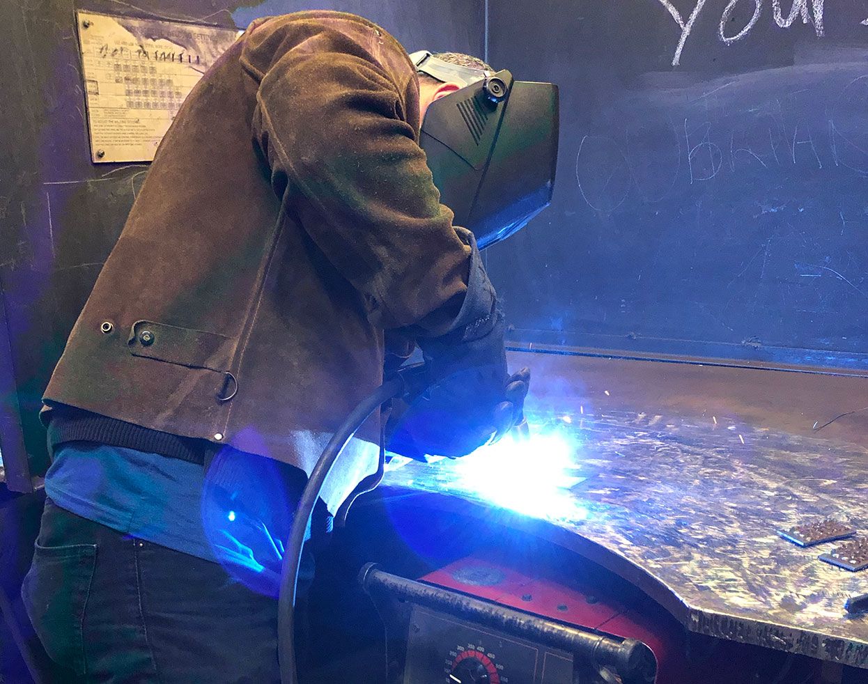 Welder working with bright blue sparks flying during metalwork process.