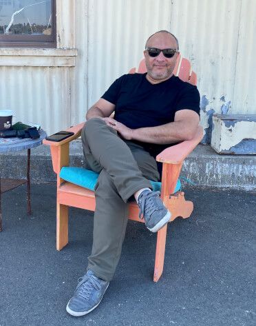 Someone relaxing in a bright orange Adirondack chair wearing sunglasses and casual attire.