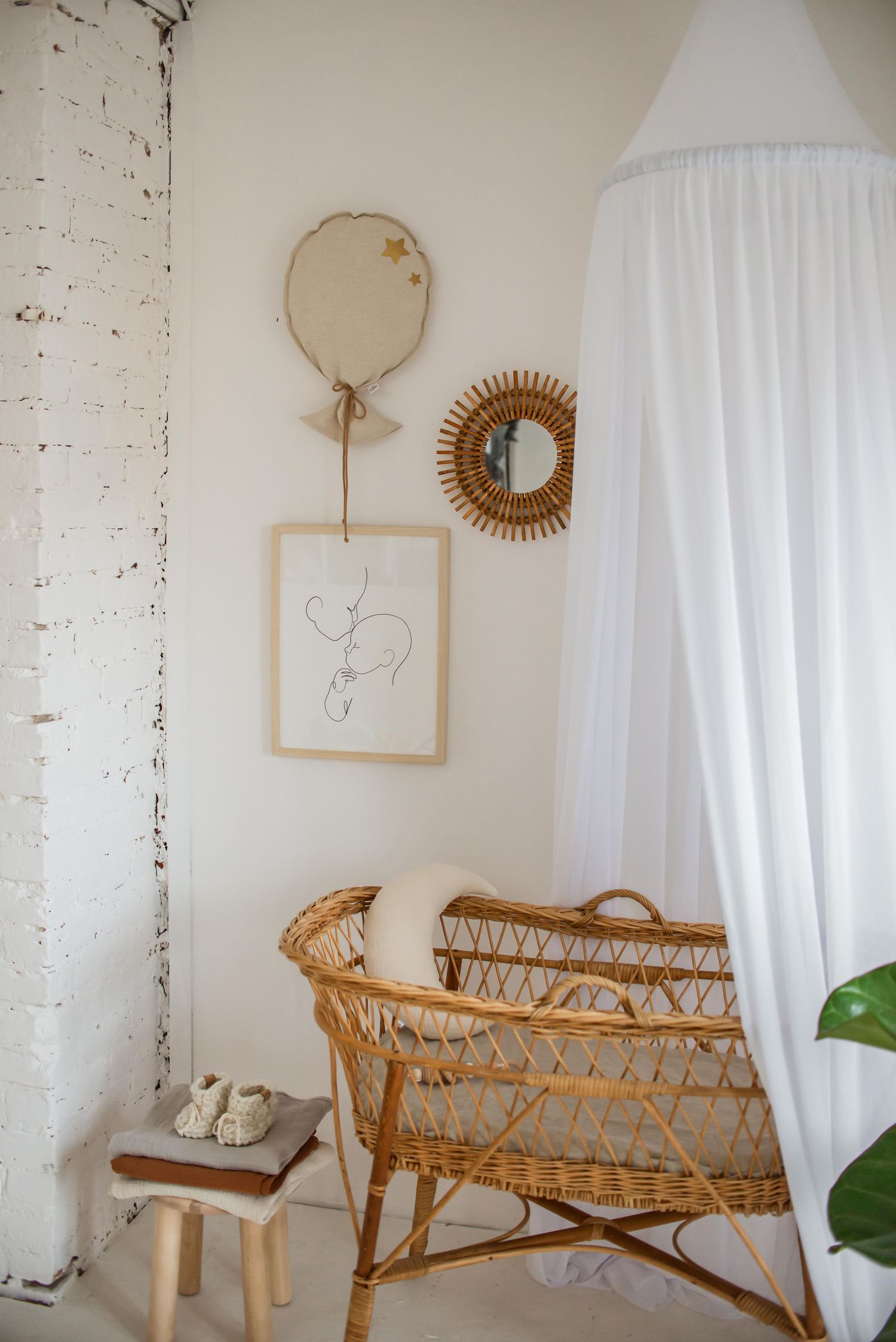 Bohemian nursery corner with rattan chair, white canopy, sunburst mirror and minimalist wall art.
