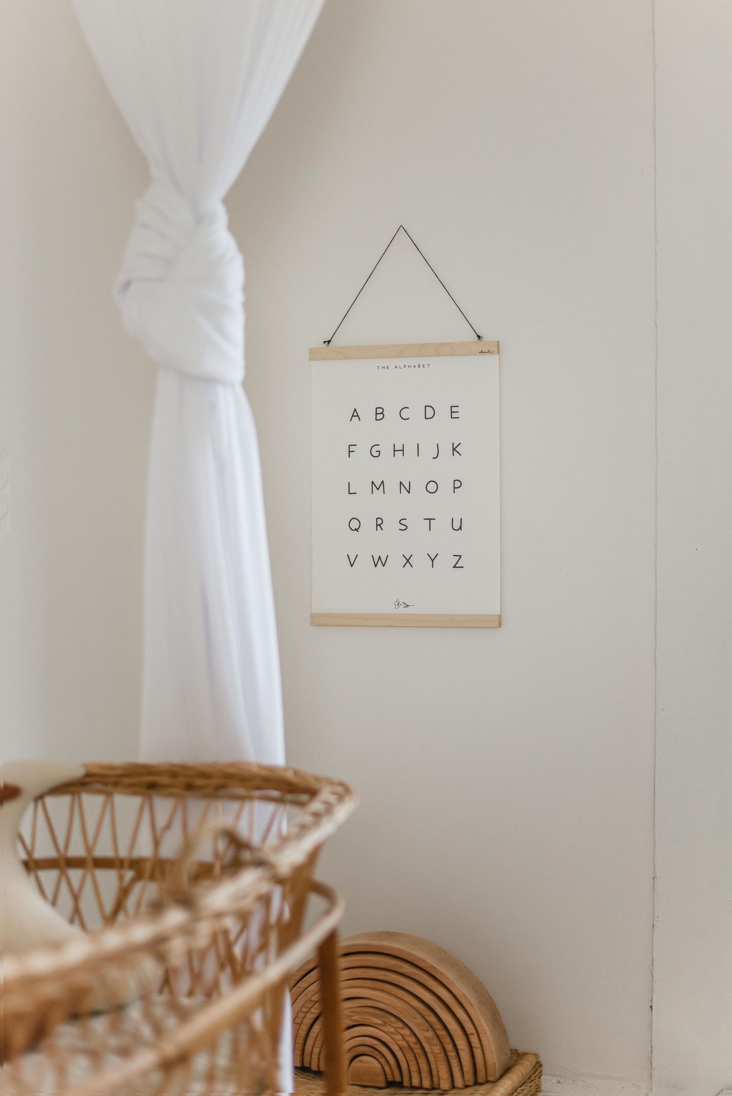 Minimalist nursery decor featuring alphabet wall art, white curtains, and natural woven baskets.