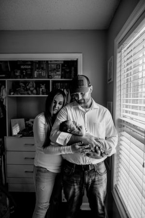 Black and white lifestyle photos of family by window in nursery.