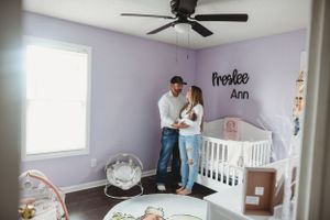 Modern nursery room with white crib, ceiling fan, and lavender walls.