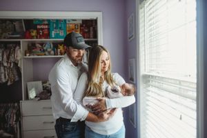 Indoor maternity photoshoot showing tender moments by a window with soft natural lighting.