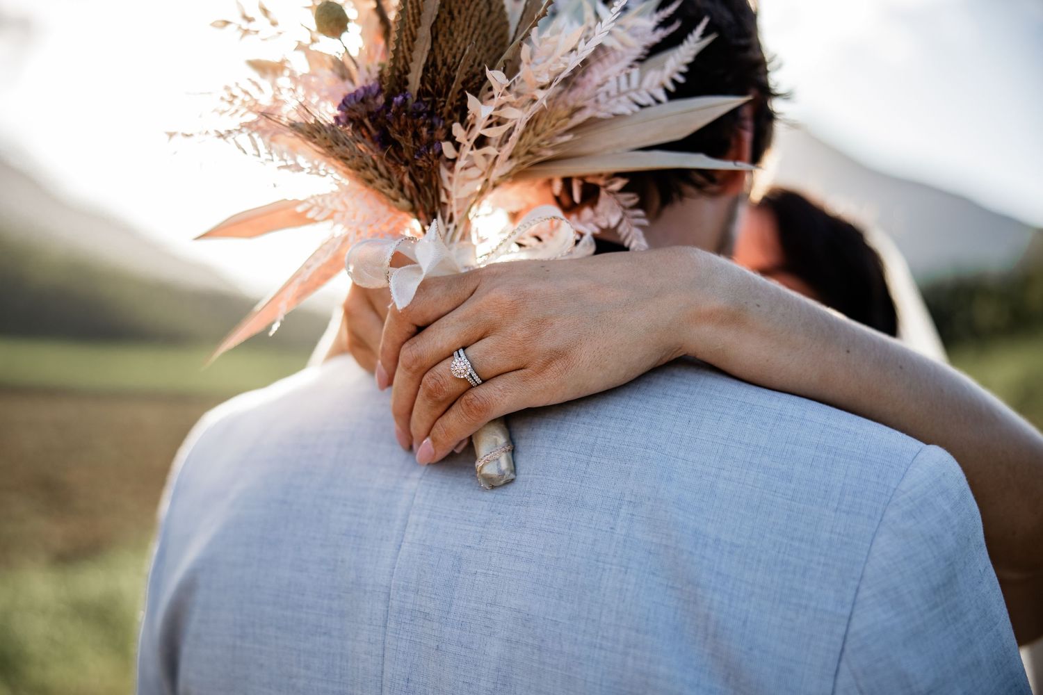 A close-up romantic embrace outdoors with white clothing and a feathered headdress against a sunlit backdrop.