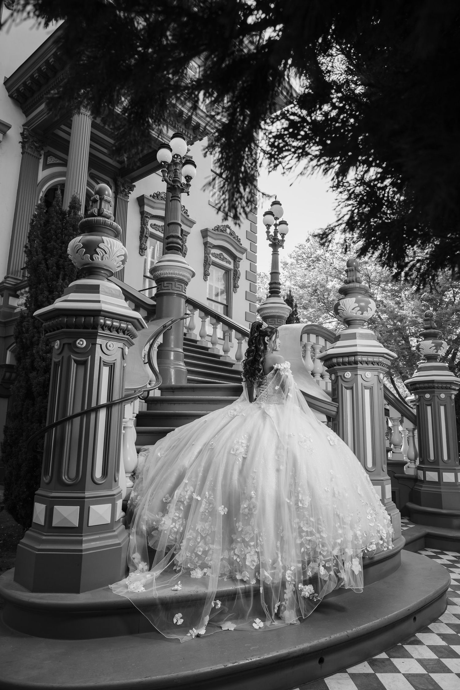 Black and white photo of an ornate wedding dress on historic Victorian mansion steps.