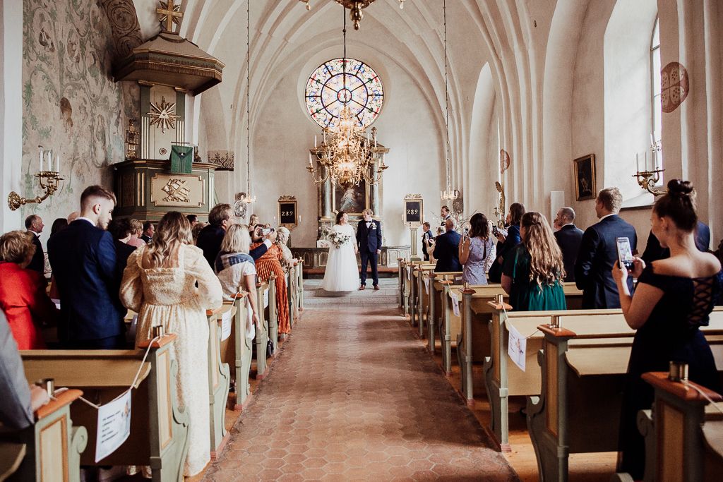 Brudpar stannar innan altargången och låter gästerna fotografera. Bröllopsfotografering i Västerås.