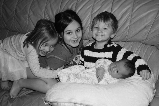 Children relaxing together on quilted bedding in black and white.